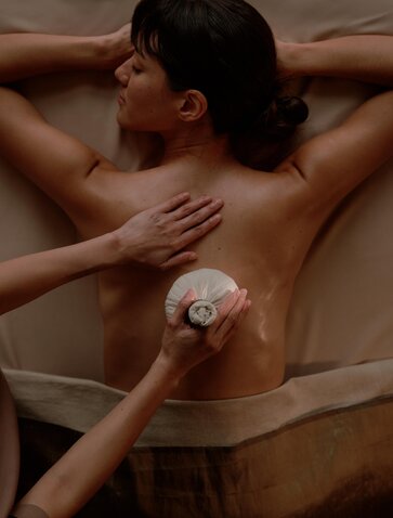 Therapist applying treatment balm to guest's back during wellness session at Aman Nai Lert Bangkok.