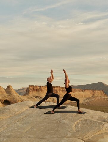 Twee gasten voeren een yogapositie uit op rotsen in de woestijn bij Amangiri resort.