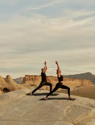 Two people practising yoga on rocky terrain at Amangiri, USA, with desert landscape and mountains in the background.
