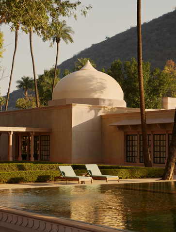 Amanbagh spa exterior with domed structure reflected in still water, framed by palm trees and stone walls.