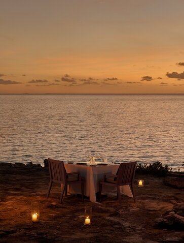 Private dining setup at Amanyara with candlelit table overlooking calm waters at sunset.