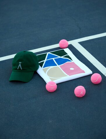 Aman Tennis Club shop display with cap, colourful geometric shapes and pink balls on court surface at Amanzoe.