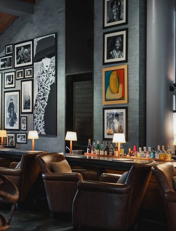 Amanoi resort bar with dark wood counter, leather seating, and framed artwork displayed on grey walls.