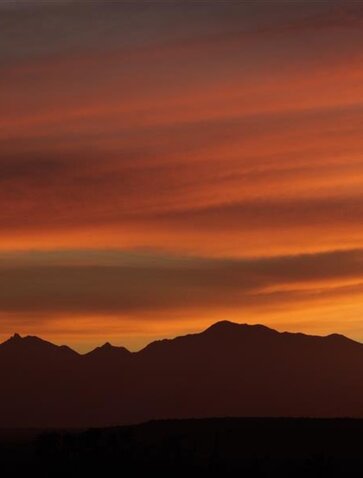 Silhouetted mountain range at Aman beneath a burnt orange sunset sky.