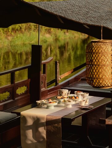 Afternoon tea service on wooden table at Amanyangyun, with views of golden-hued landscape through open-sided pavilion.