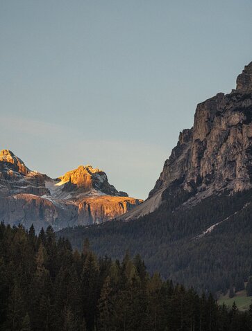 Golden sunlight illuminates peaks above forested valleys at Aman Rosa Alpina in the Dolomites.