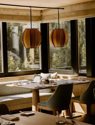 Sala da pranzo presso Aman Rosa Alpina con tavolo in legno, sedie nere e lampade sospese in rame.