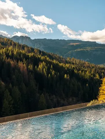 Outdoor swimming pool overlooking forested Alpine valleys at Aman Rosa Alpina resort, Italy.