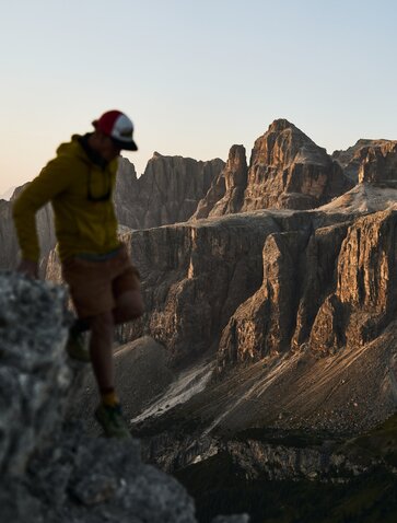 Hiker in green jacket gazing towards dramatic mountain peaks at Aman Rosa Alpina resort, golden hour light.