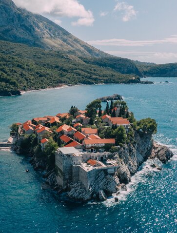 Aerial view of Sveti Stefan island with terracotta-roofed buildings perched on rocky outcrop in turquoise waters, Montenegro.