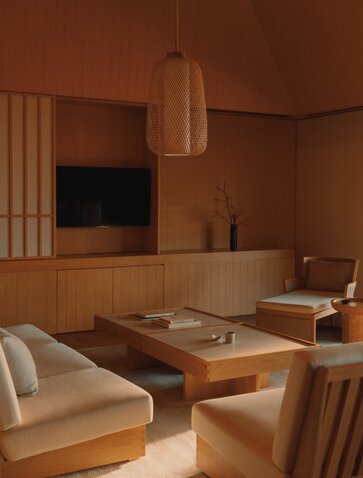 Spacious principal bedroom at Amanemu resort with warm wood panelling, low platform bed, and pendant lighting.