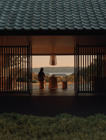 Amanemu resort's Welcome Pavilion at dusk, wooden doors open to reveal a warm interior with traditional Japanese architecture.