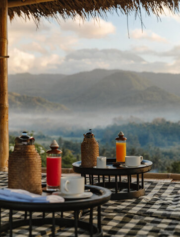 Sunrise breakfast at Amankila with coloured bottles and traditional setup overlooking misty Balinese mountains.