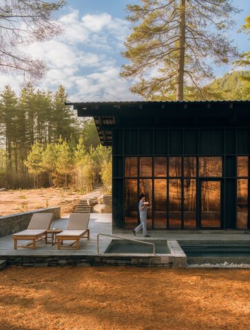Spa house at Amankora's Paro Lodge with illuminated interior, wooden deck and forest setting at dusk.