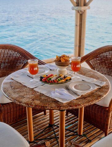 Floating bar at Amanpulo with woven chairs, fresh fruit and drinks on a round table overlooking turquoise waters.