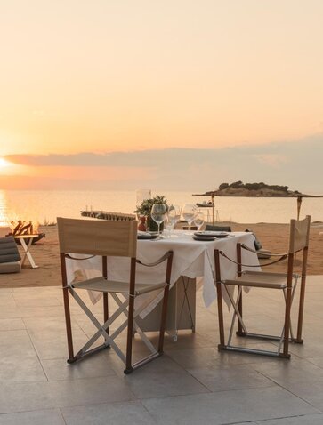 Dining table and chairs set on a terrace at Amanzoe at sunset, overlooking the Aegean Sea.