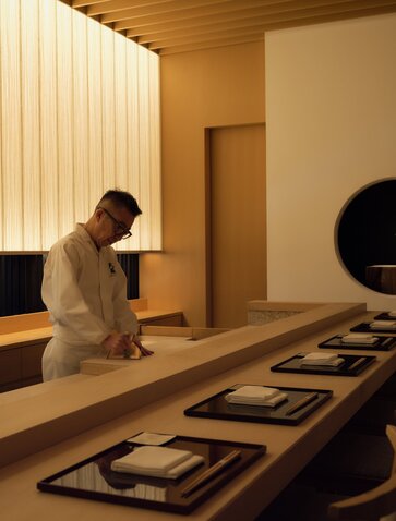 Dining venue at Aman Tokyo with traditional Japanese design and warm wooden finishes, featuring a long table and seated server.