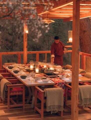 Outdoor dining setup at Amankora with candlelit table overlooking forest and stream at dusk.
