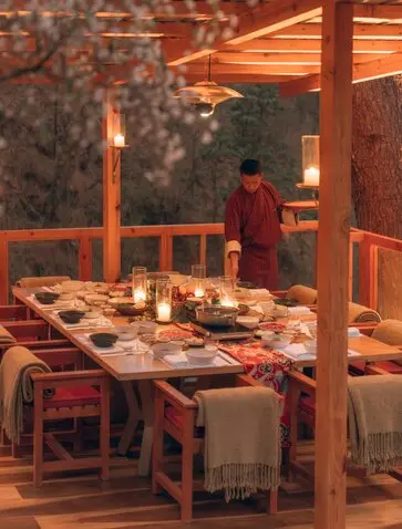 Outdoor dining setup at Amankora with candlelit table overlooking forest and stream at dusk.