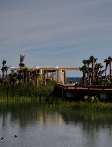 Beachfront casita at Amanvari with traditional wooden boat moored along tranquil waterway lined with palm trees.