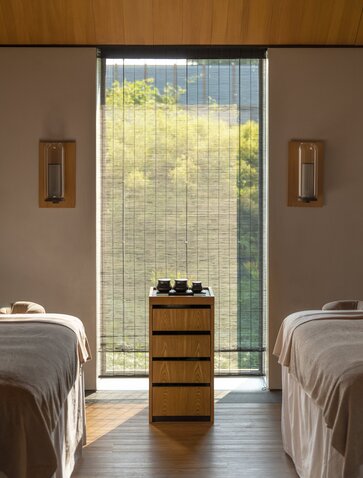 Spa treatment room at Amanyangyun with twin massage beds and wooden storage, overlooking garden through large window.