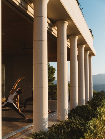 Colonnade with tall columns at Amanzoe, Greece, overlooking mountains under clear sky.