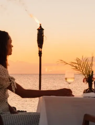 Woman seated at beachside dining table at Amanyara at sunset, overlooking Caribbean waters.