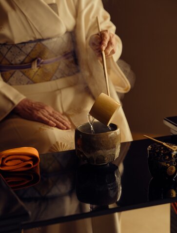 Traditional tea ceremony preparation at Aman Kyoto, with hands holding a bamboo whisk over matcha bowl.