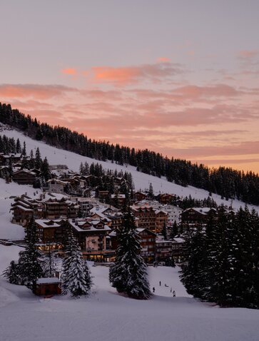 Aman Le Mélézin exterior at dusk, snow-covered alpine landscape beneath a pink-streaked sky.