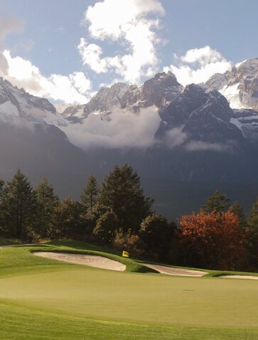 Snow-covered mountains rise beyond a golf course fairway at Amandayan, China.