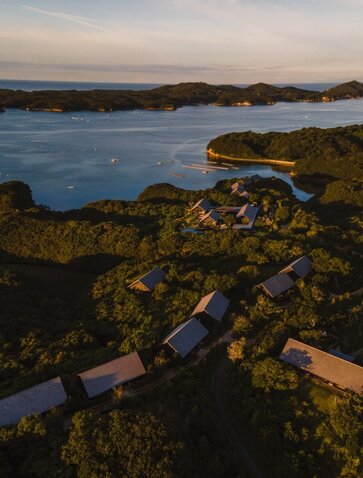 Amanemu resort nestled among moss-covered rocks along Japan's coastline at dusk.