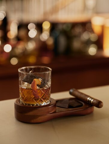 Rum cocktail with ice at Amanera, Dominican Republic, paired with cacao nibs on wooden coaster.