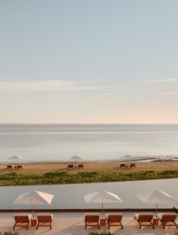 Amanvari's seafront terrace with loungers overlooking calm coastal waters at dusk.