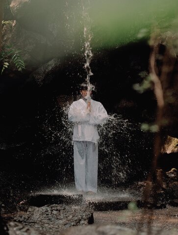 Guest participating in a waterfall purification ritual at Amanemu, water cascading over white clothing.
