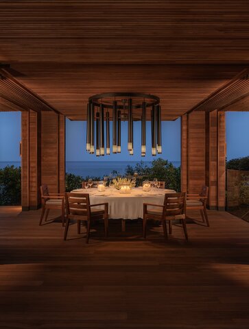 Amanoi Ocean Pool Residence dining area at night, with wooden architecture framing a table set for dinner overlooking the sea.