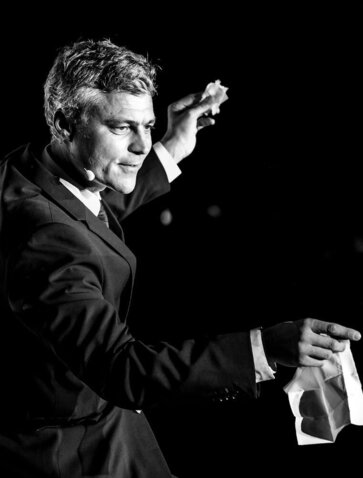 Man in dark jacket gestures while speaking at Amanoi during New Year celebration.