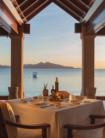 Beachclub dining table at sunset, framing volcanic island views across calm waters at Amanpulo, Philippines.