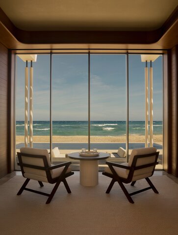 Two wooden chairs facing the sea view through floor-to-ceiling windows at Amanvari beachfront casita.
