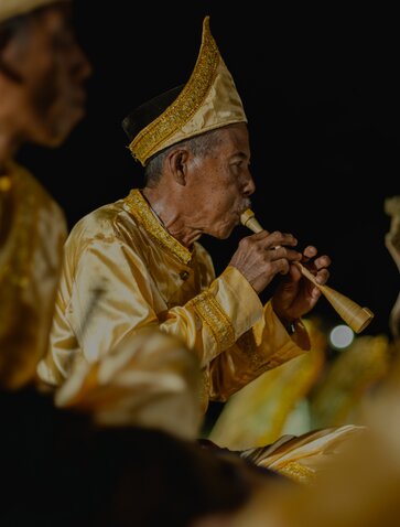 Indonesian performer in traditional gold headdress playing wind instrument at Amanwana.