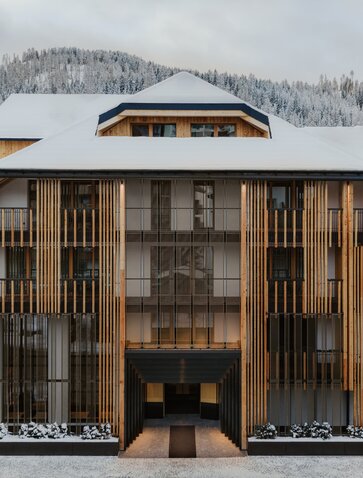 Aman Rosa Alpina entrance with wooden façade and snow-covered mountains beyond.