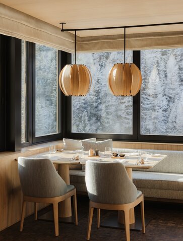 Heritage Room at Aman Rosa Alpina: desk with two wooden pendant lights and upholstered chairs overlooking snowy Alpine landscape.