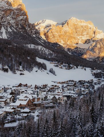 Snow-covered mountain village at Aman Rosa Alpina with golden peaks at sunrise, Italian Alps.