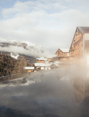 Aman Rosa Alpina's outdoor pool with Alpine peaks and morning mist in the Italian Dolomites.