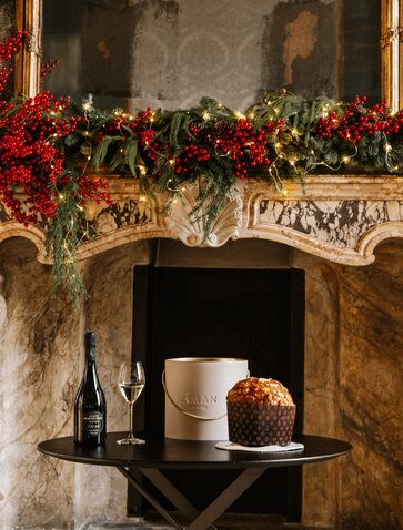 Festive fireplace display at Aman Venice featuring panettone and champagne beneath garland-draped mantelpiece.
