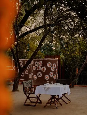 Forest dinner setting at Aman-i-Khas with candlelit table beneath trees at dusk.