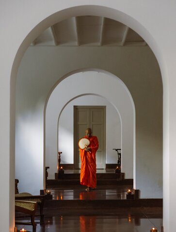 Monk in red robes within arched corridor at Amangalla, Sri Lanka spa and wellness retreat.