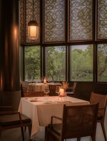 Intimate dining room at Amanyangyun with round table, forest views through large windows, and warm pendant lighting.
