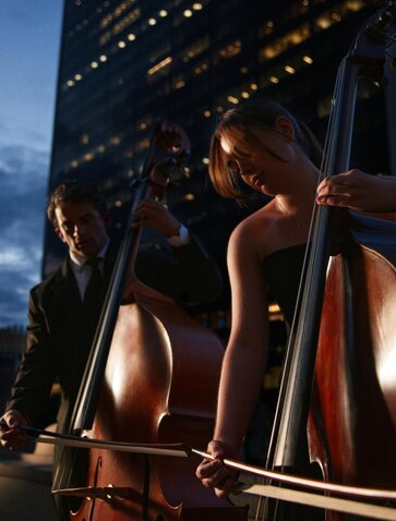 Cellos displayed against illuminated architectural framework at Aman New York, evening light.