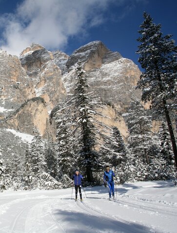 Snow-covered peaks and evergreens frame two figures cross-country skiing at Aman Rosa Alpina in the Dolomites.