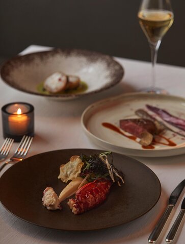 Plats festifs présentés à Aman Tokyo, avec verre de vin blanc et bougies allumées.